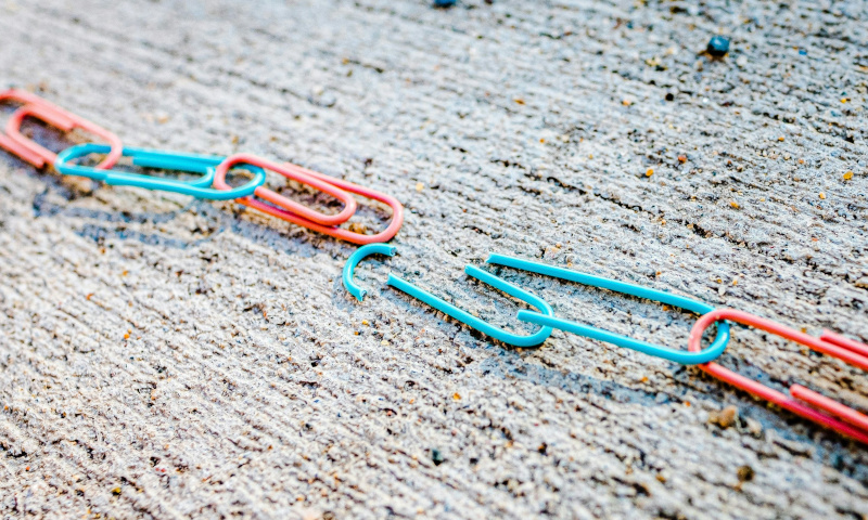 Paper clips on the ground with one unlinked and broken, a photograph by Jackson Simmer